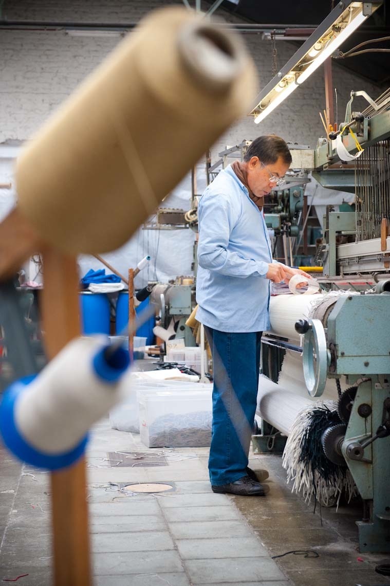 Craftsman working at a vintage loom with spools of leather thread in Atelier Charles Schambourg's workshop.