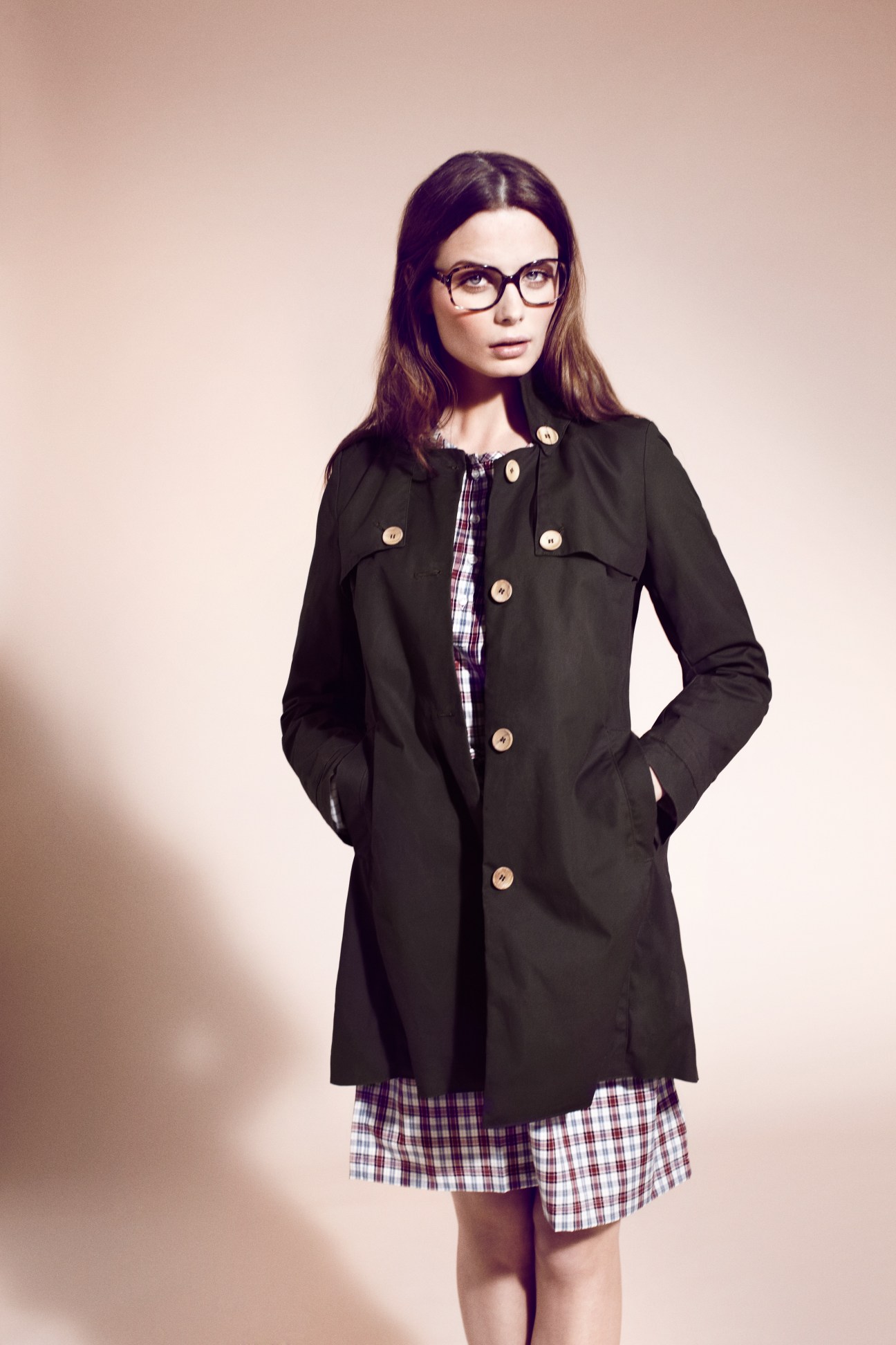 Woman wearing a black Oliver Spencer coat over a purple plaid dress with Prada glasses.