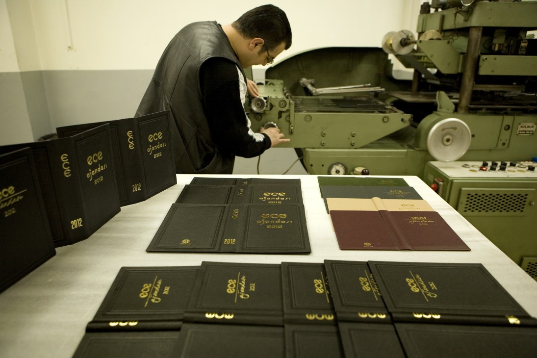 Worker operating vintage printing machinery to brand Ece diaries with gold lettering and logo.