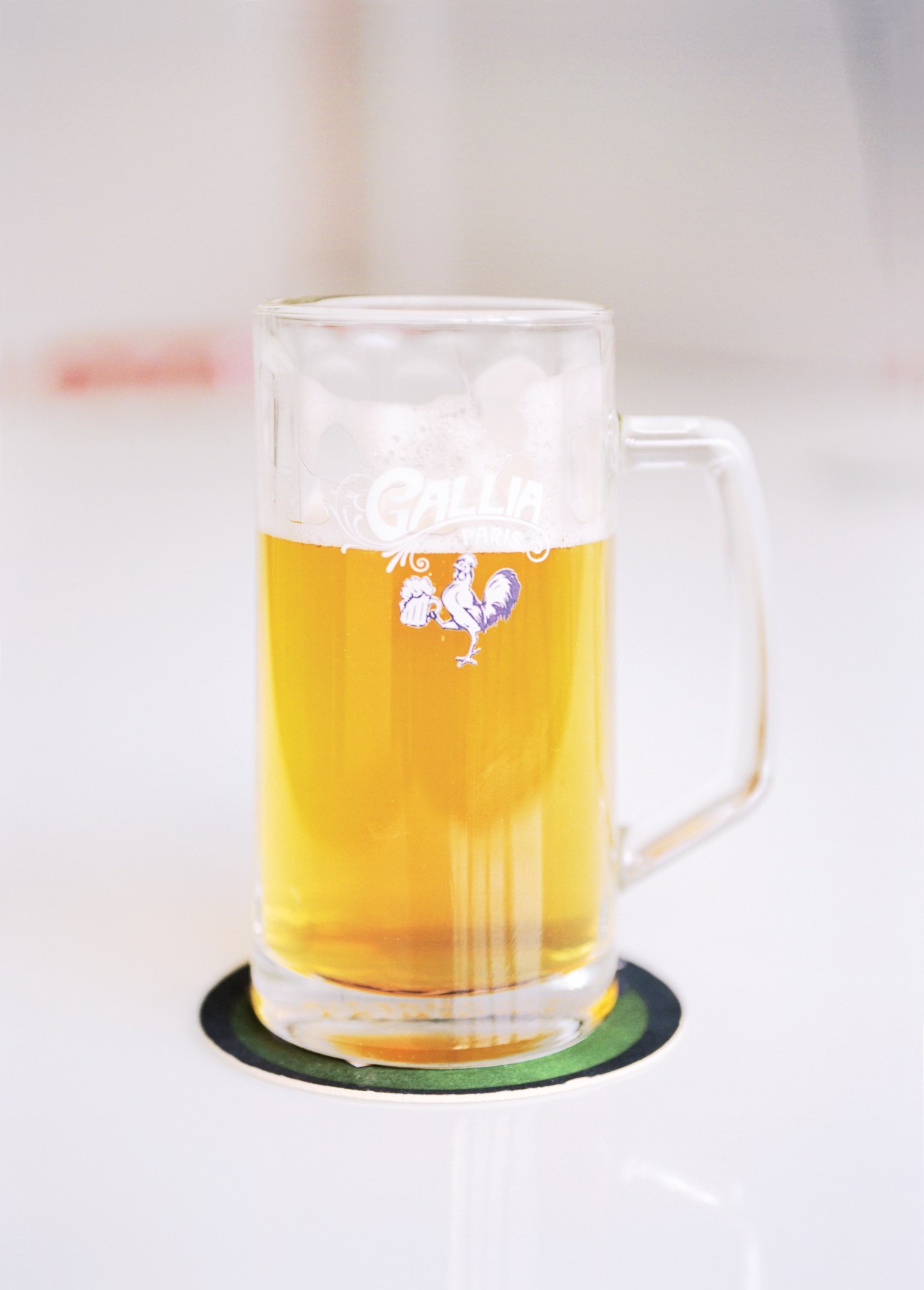 A glass of Gallia beer with the revived brand's cockerel logo and Guimard typeface displayed on the glass.