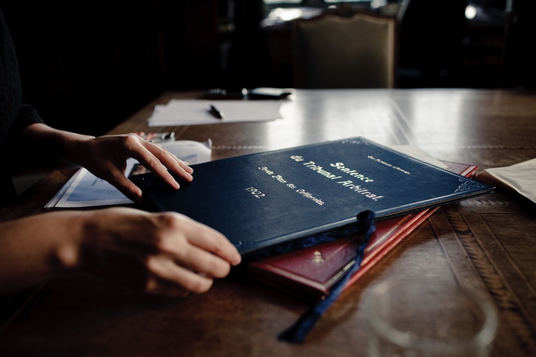 Hands examining a blue leather-bound casebook on a wooden table with other legal documents nearby.