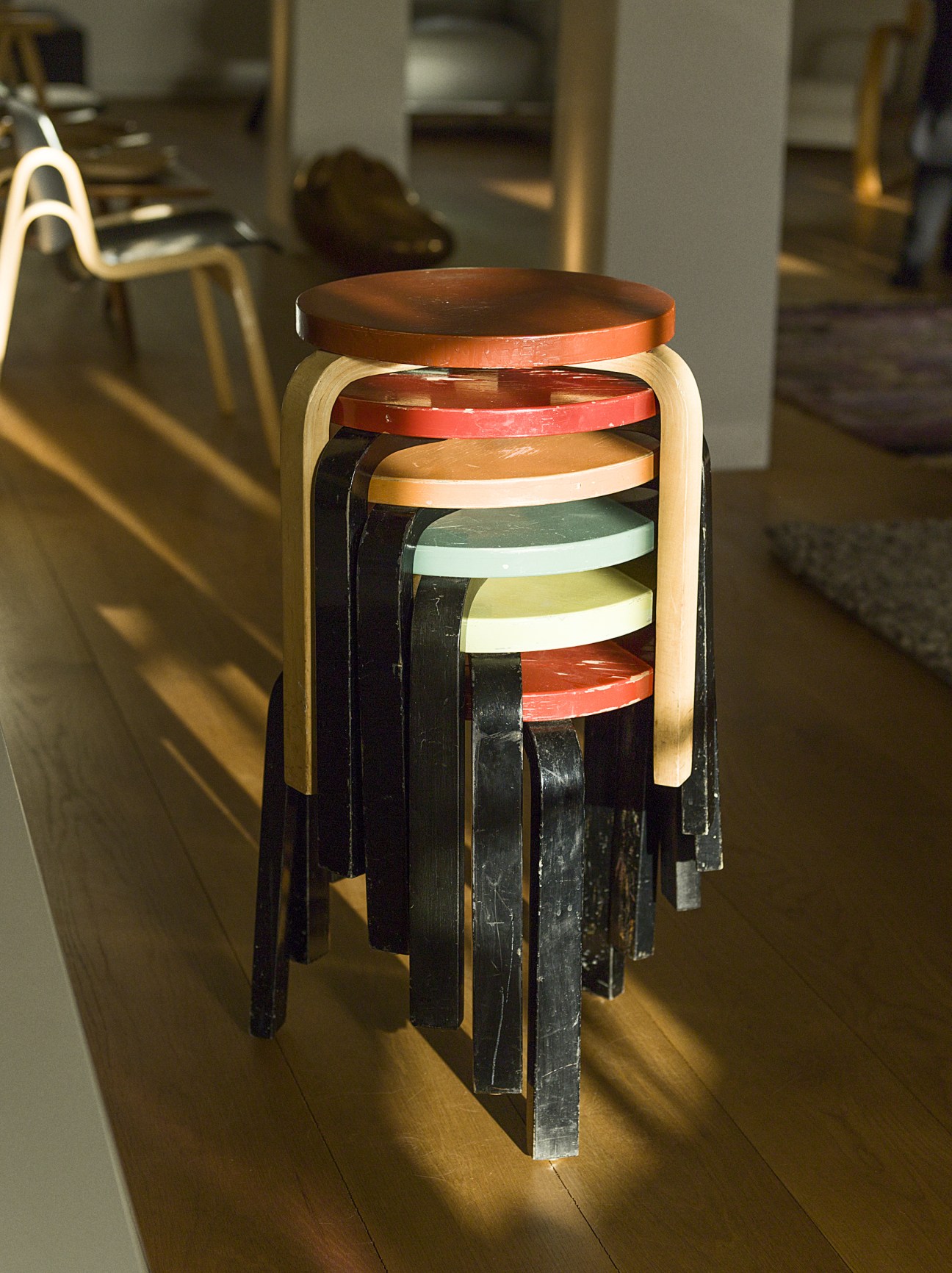 Stool 60s by Alvar Aalto stacked stools with colorful wooden seats in various hues.