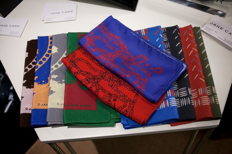 Jane Carr Homme scarves in various colors displayed on a white surface with brand cards nearby.