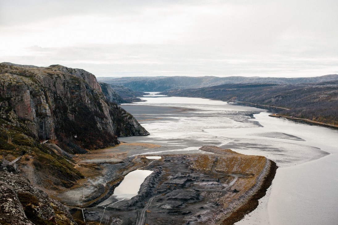 Arctic fjord with rocky cliffs, frozen water, and mining operations visible in the valley below.