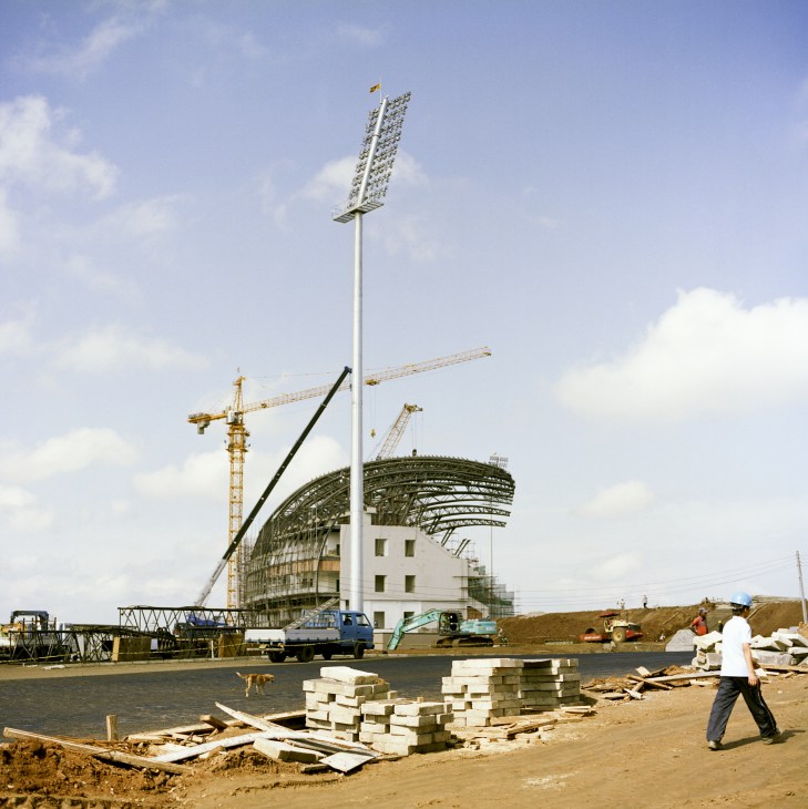 The Suriyawewa International Cricket Stadium under construction with cranes, steel framework, and a tall floodlight tower on a construction site.