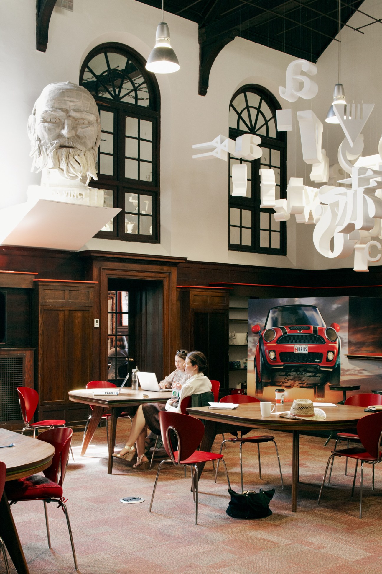 Interior of VIA advertising agency in a converted Portland library with high ceilings, classical busts, and modern red chairs.