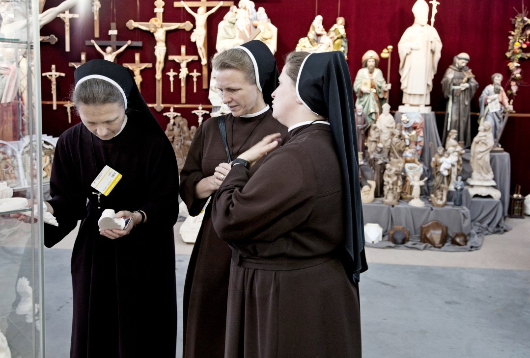 Three nuns in black habits browse religious statues and crucifixes displayed at SacroExpo trade fair.