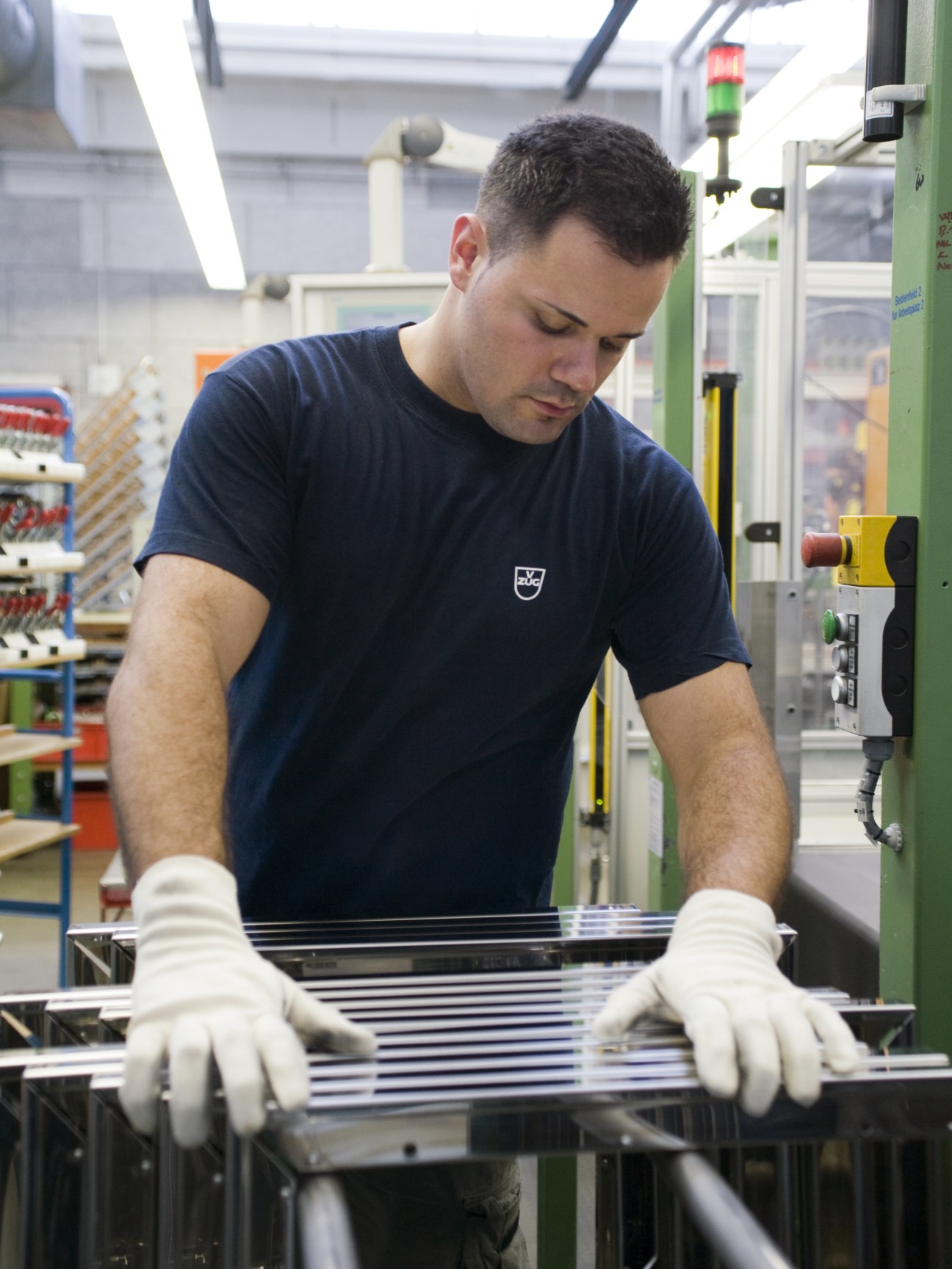 A V-Zug engineer in a navy t-shirt inspects stacked glass oven doors on a factory workstation.