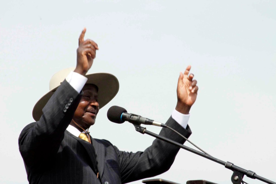 Man in dark suit and cowboy hat speaking passionately at microphone with raised hands.