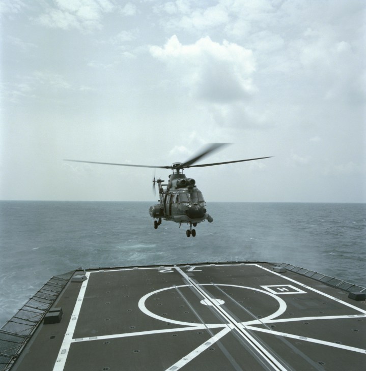 A Super Puma helicopter hovers above the landing deck of the RSS Stalwart frigate during a landing operation.