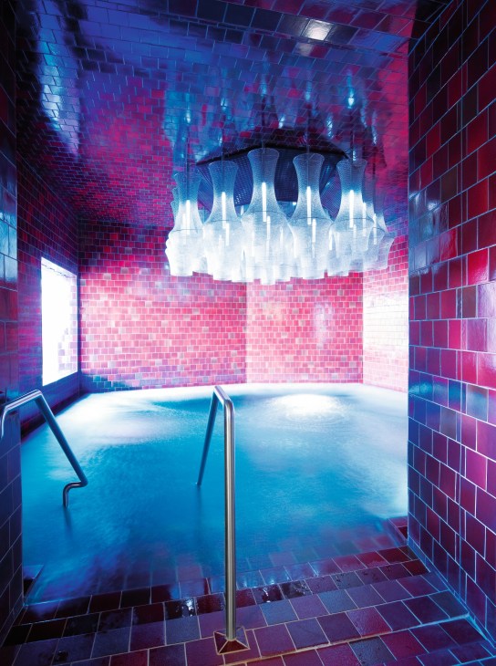 Modern spa pool with pink and blue tile walls and illuminated ceiling fixture at Samedan spa.