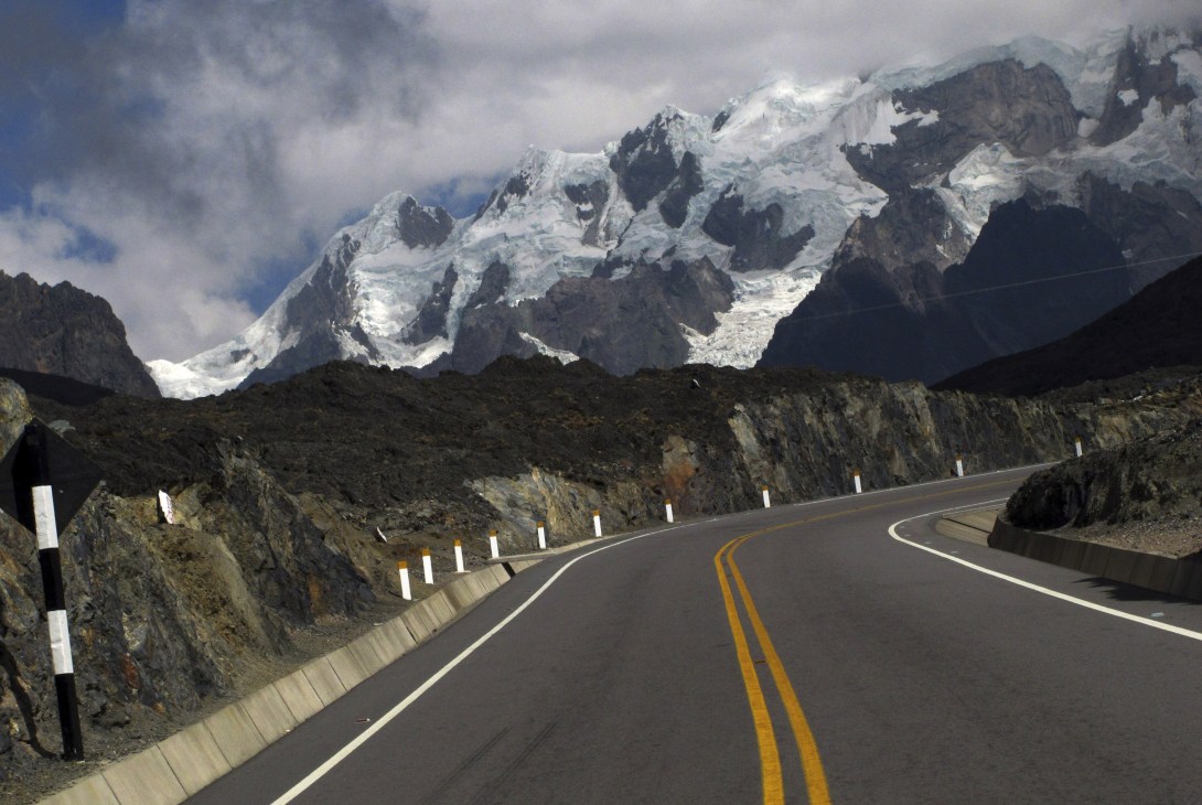 A modern highway curves through mountains with snow-capped peaks in the background.