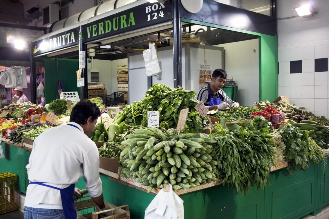 Vendors sell fresh vegetables and produce at a market stall with green signage reading 'Frutta & Verdura' in Rome's Esquilino neighbourhood.