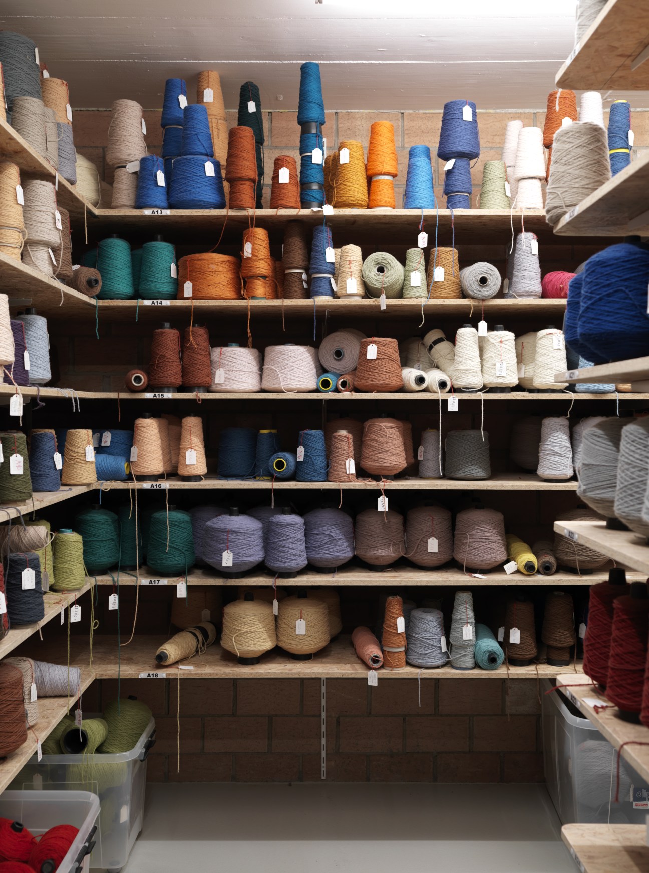 Shelves displaying spools of dyed wool in various colors including blue, orange, cream, and purple at Kramis carpet workshop.