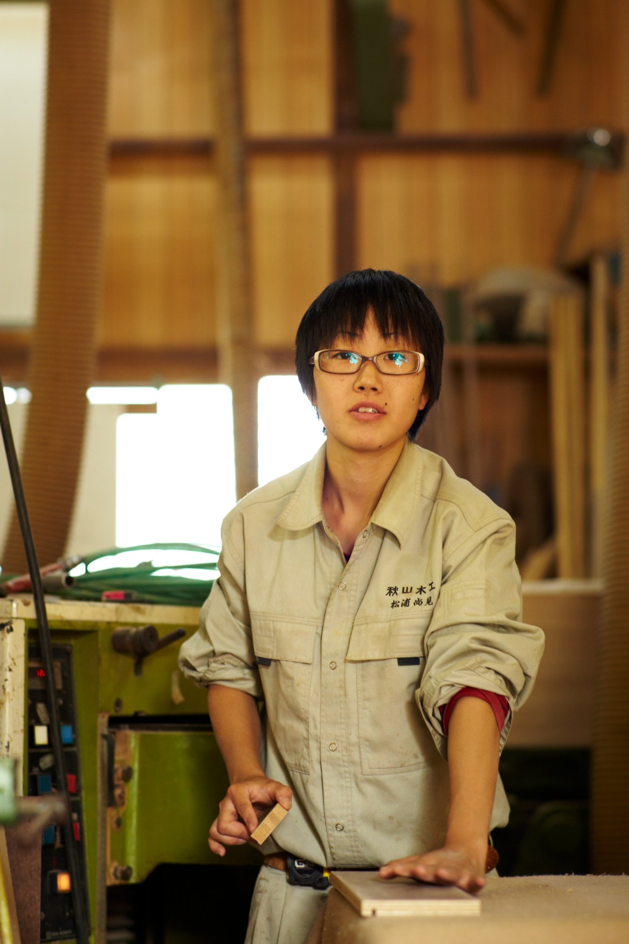 Young apprentice in beige work uniform with glasses at furniture workshop.