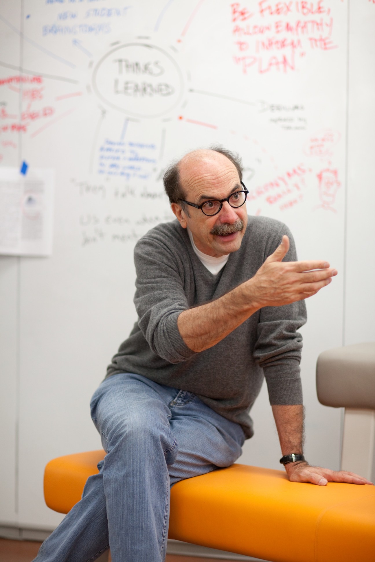 David Kelley, founder of Stanford's d.school, gestures while speaking in front of a whiteboard with design sketches.