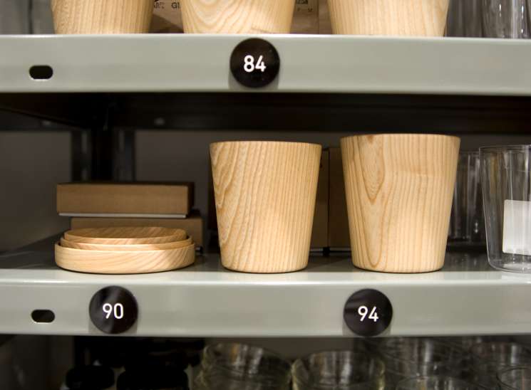 Wooden cups with lids and glass lab bottles displayed on metal shelves in Good Design Shop.