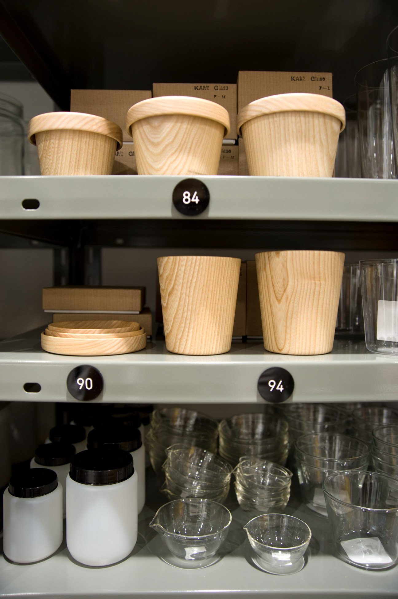 Wooden cups with lids and glass lab bottles displayed on metal shelves in Good Design Shop.