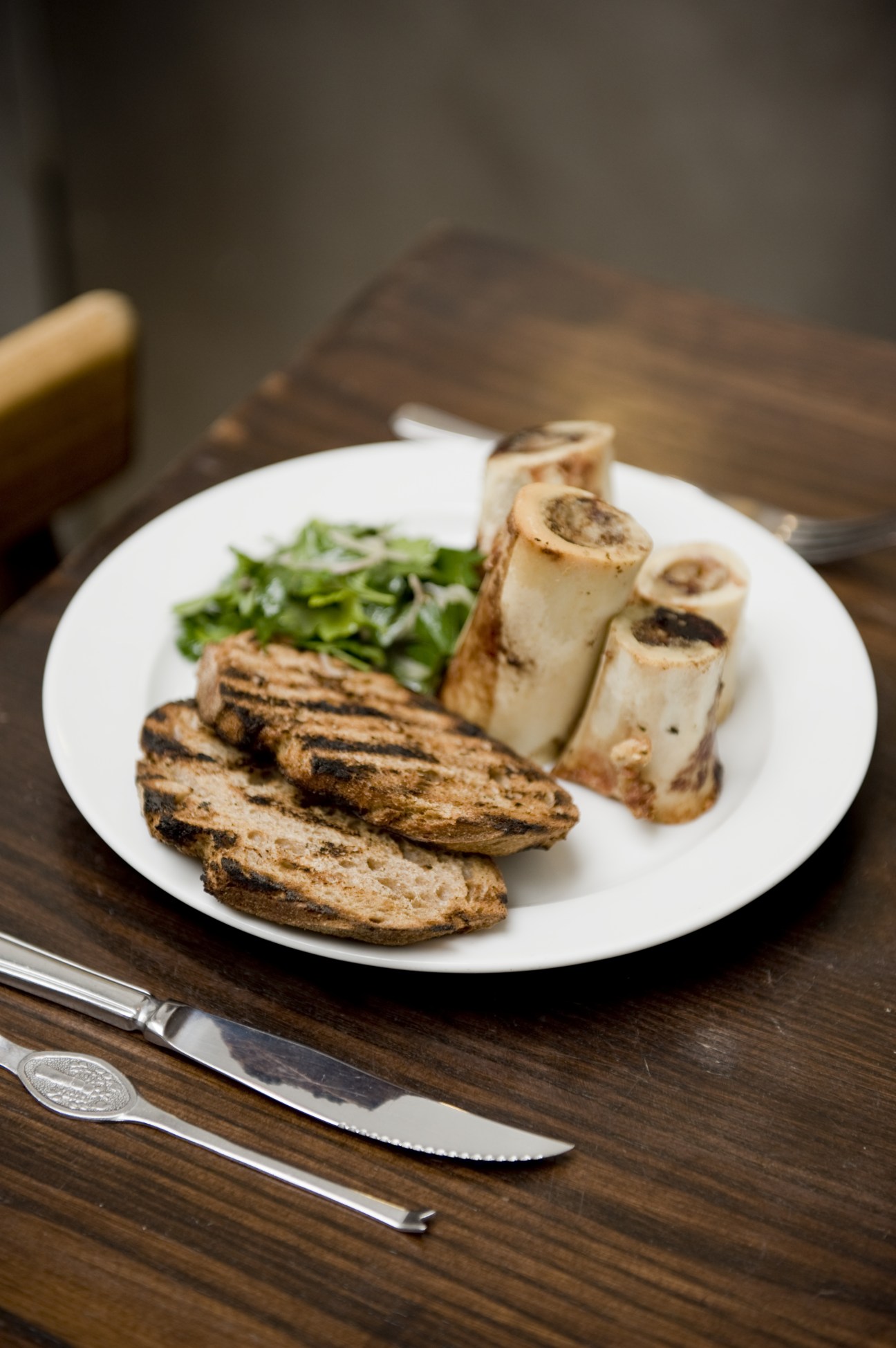 Roasted bone marrow bones with parsley salad and toasted bread on a white plate.