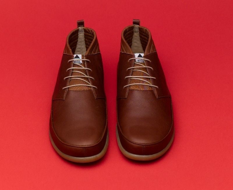Pair of Volta brown leather sneakers with laces on red background.