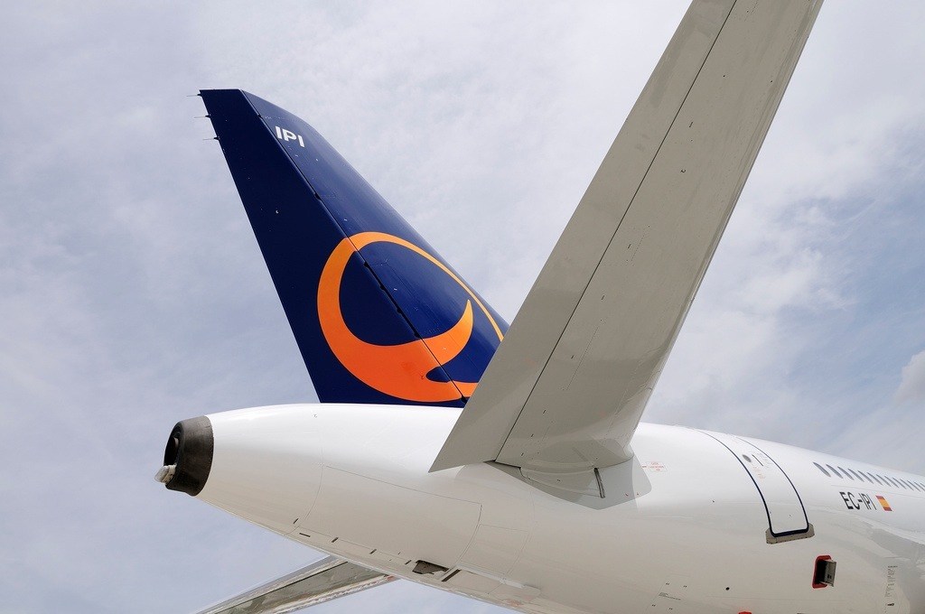 Tail fin of Spanair aircraft with blue and orange logo against cloudy sky.