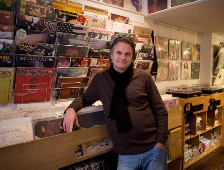 Man standing at counter in Amsterdam record shop surrounded by vinyl records and display shelves.