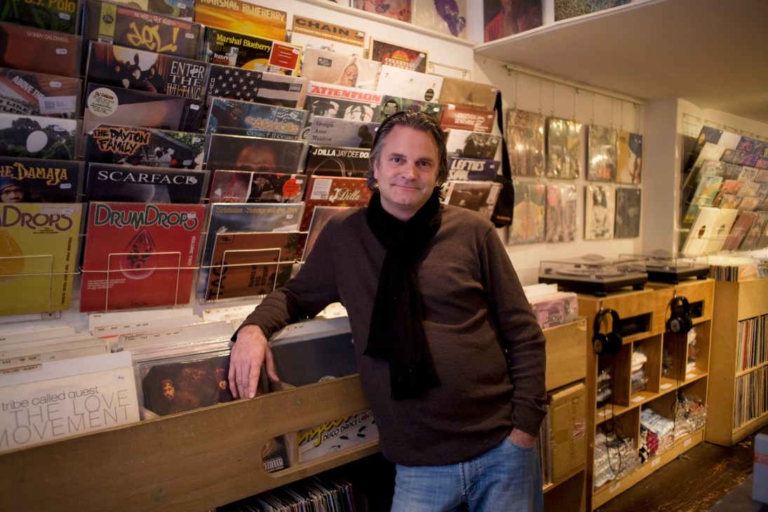 Man standing at counter in Amsterdam record shop surrounded by vinyl records and display shelves.