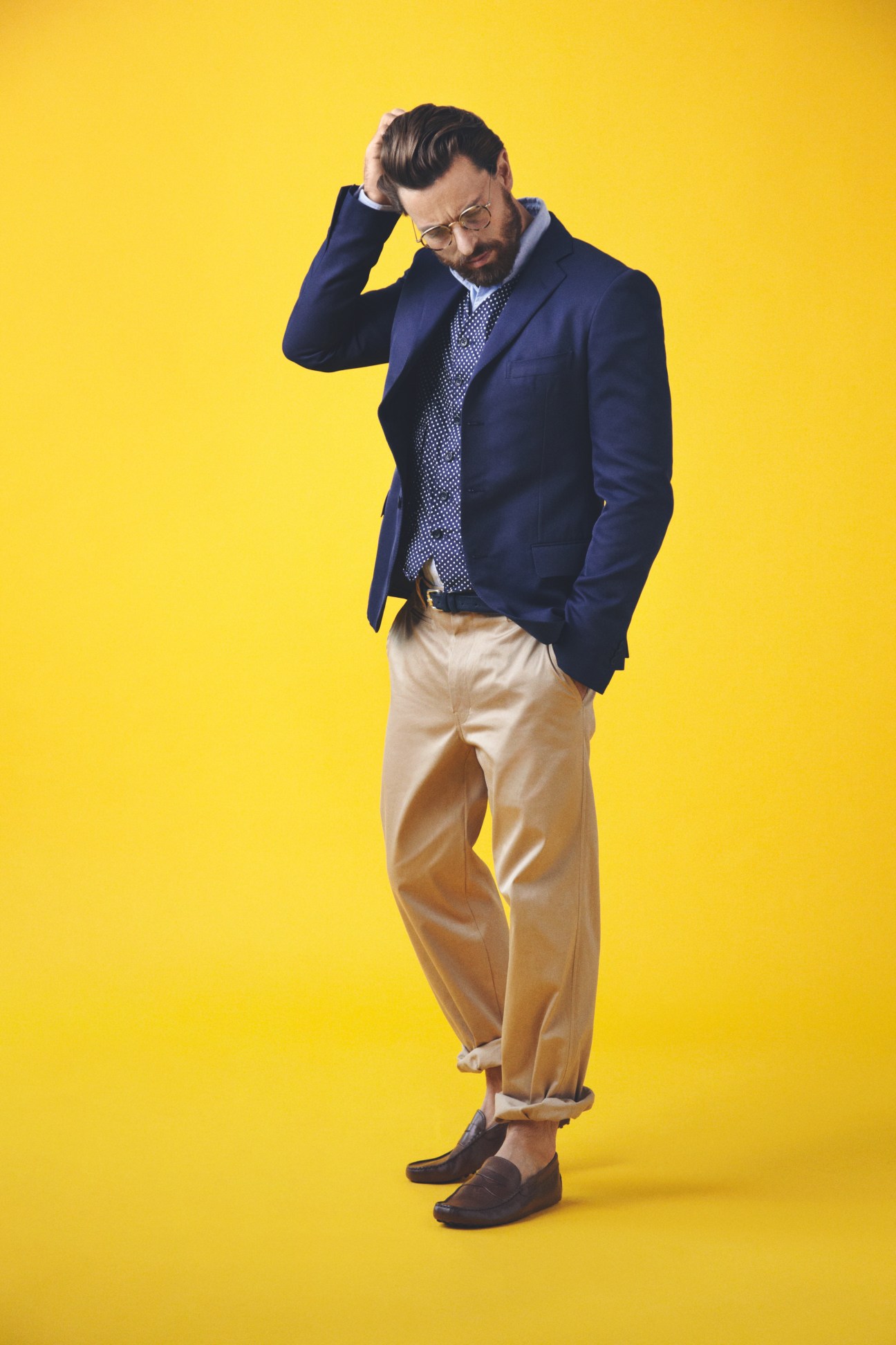Man in navy Bottega Veneta jacket, patterned shirt, and tan trousers against yellow background.