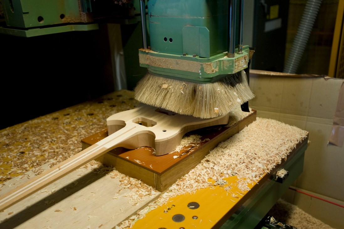 A CNC machine with a rotating brush cuts guitar body wood at Yamaha factory.