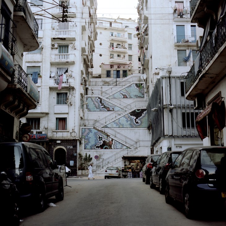Narrow Algiers street lined with white apartment buildings and decorated staircase with mosaic tilework.