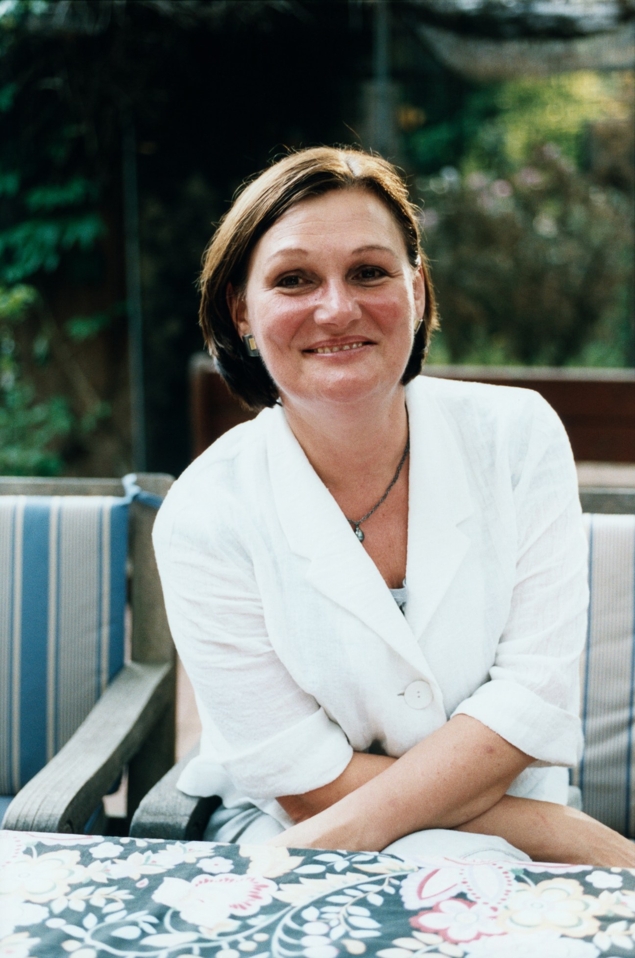 Woman in white blazer smiling outdoors with garden background