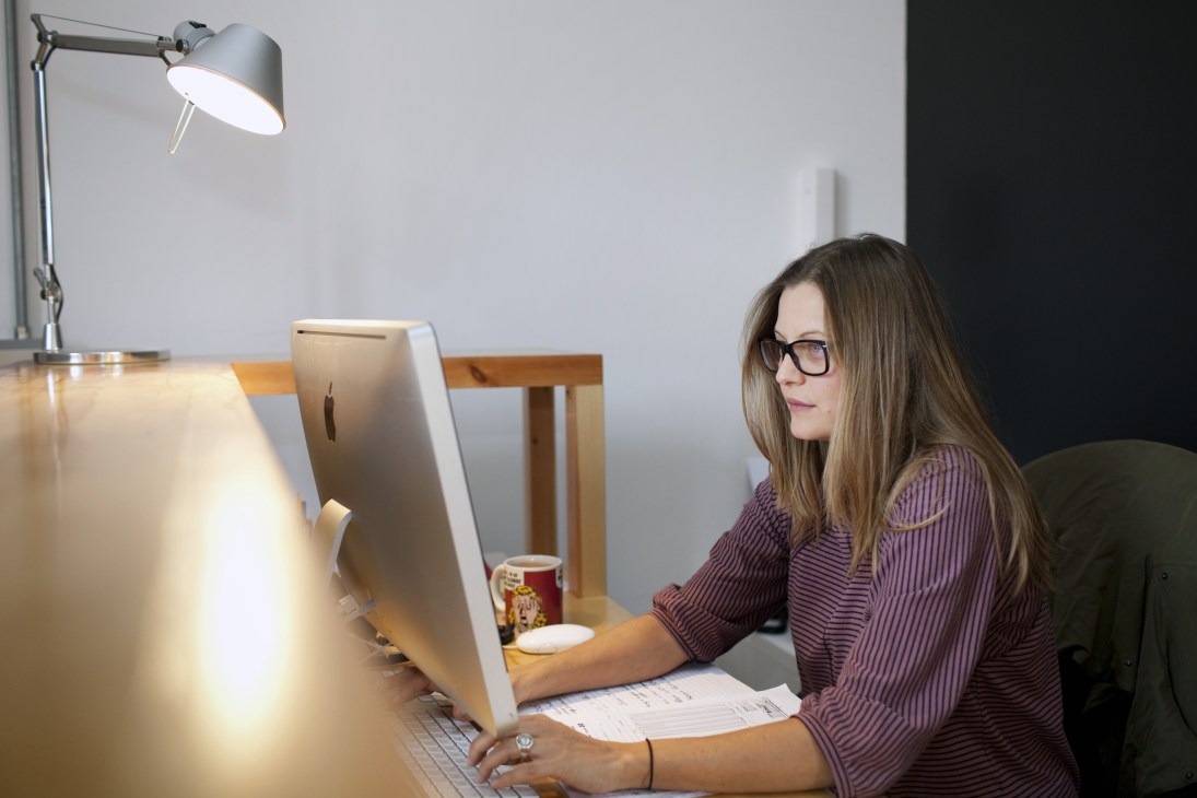 Woman working at a desk with a computer in a modern office space with industrial lighting.