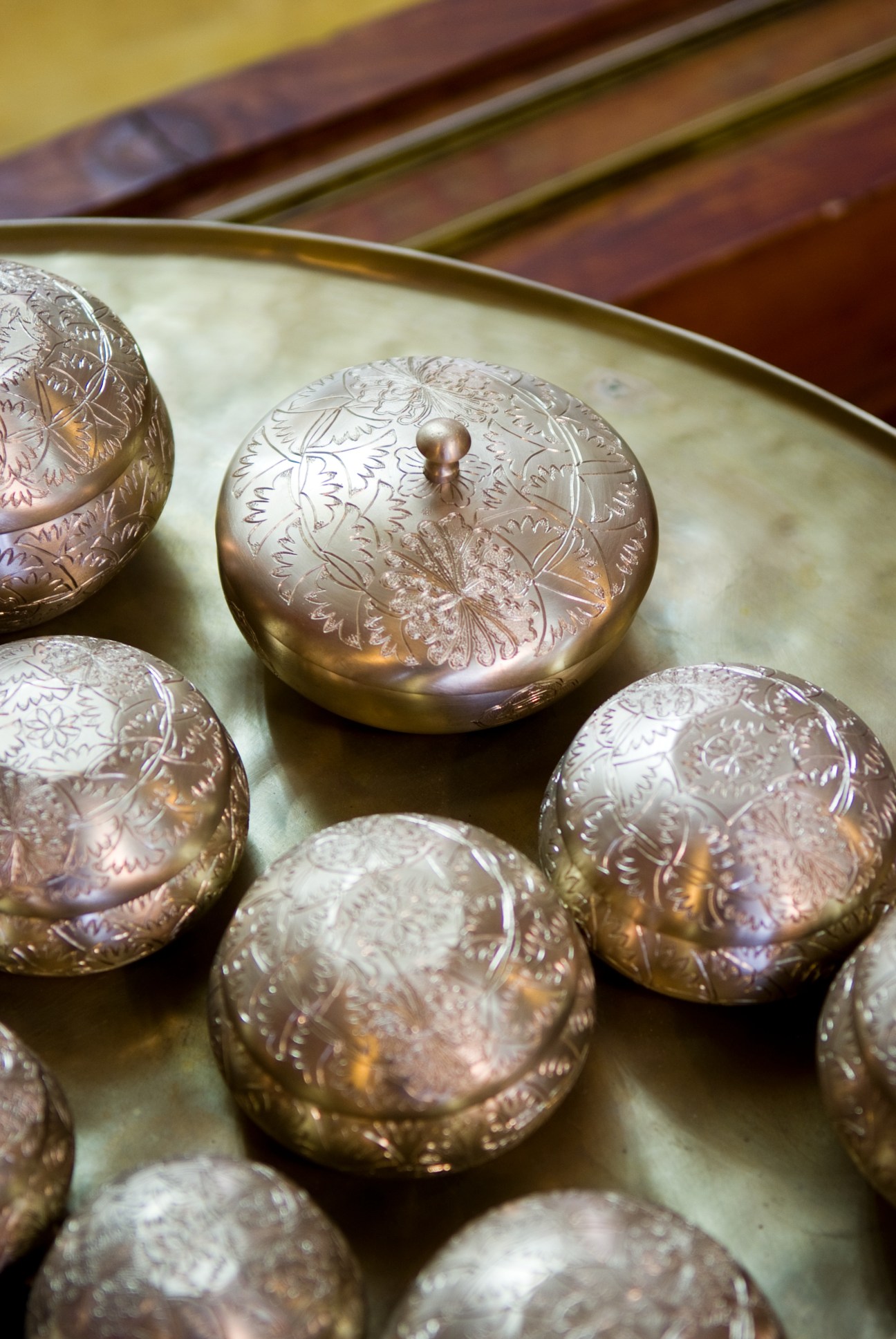 Engraved bronze bowls with white-gold finish and intricate floral patterns displayed on a pale green surface.