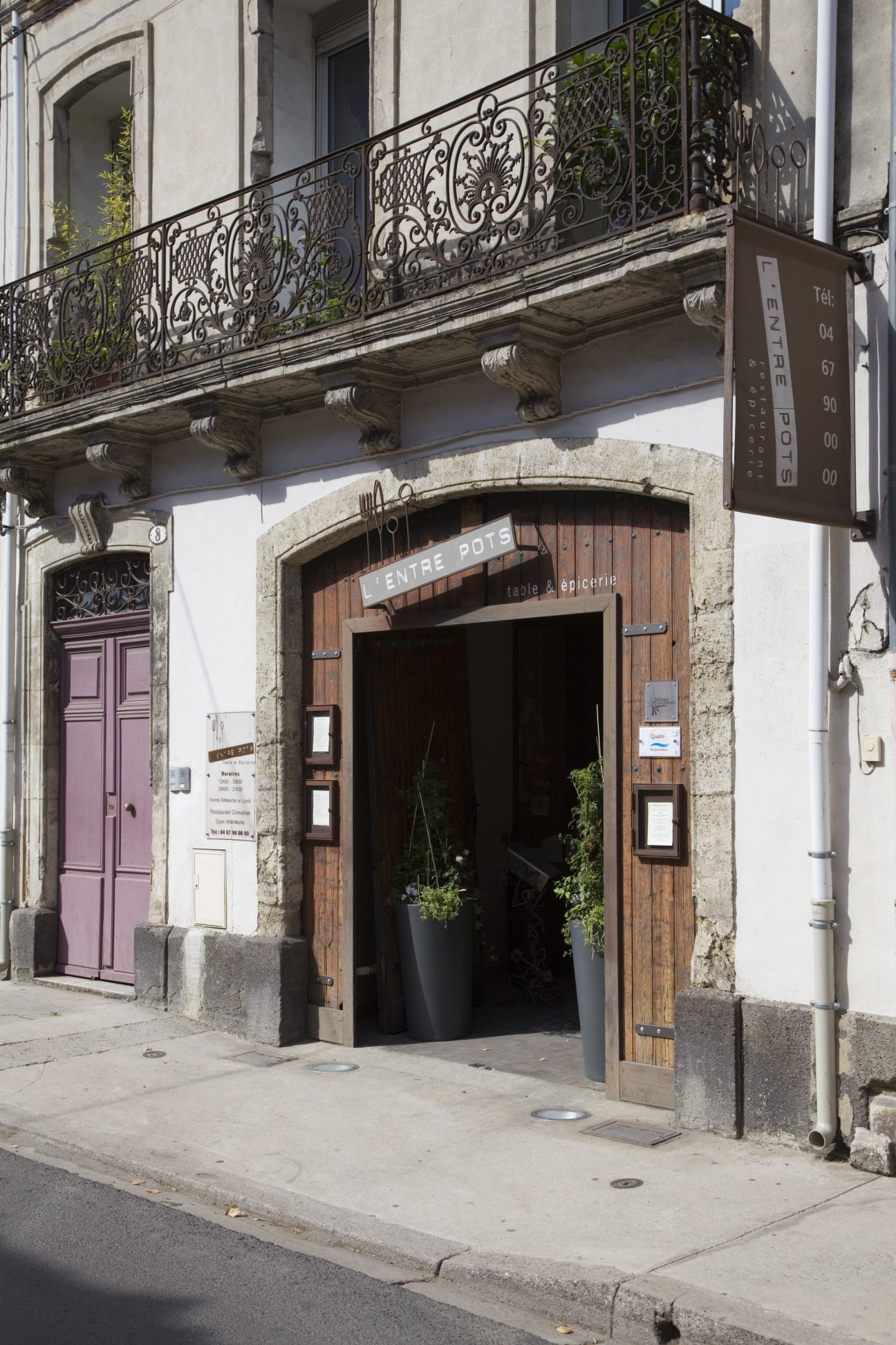 The entrance to L'Entre Pots restaurant in Pézenas, France, with ornate ironwork balcony and wooden door.