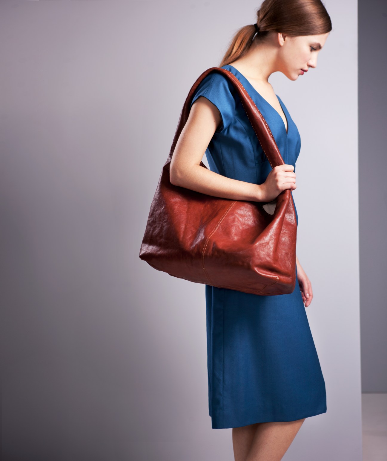 Woman wearing blue dress carrying a burgundy leather shoulder bag from Genten.