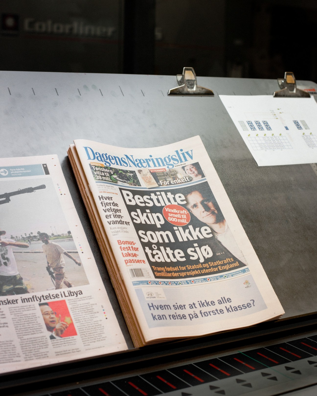 Dagens Næringsliv newspaper front page displayed on a printing press with metal clamps.