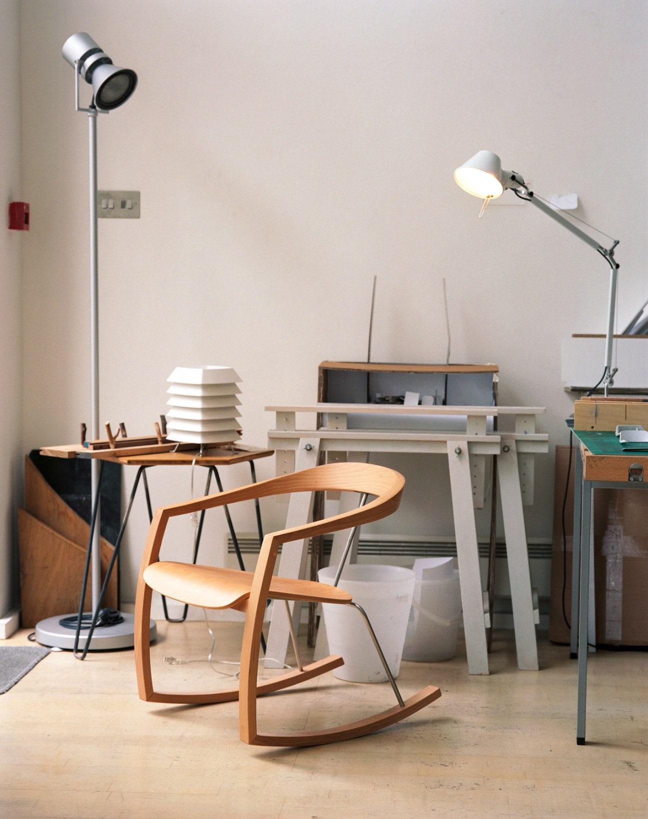 Wooden rocking chair with curved arms in a design studio filled with models and prototypes.