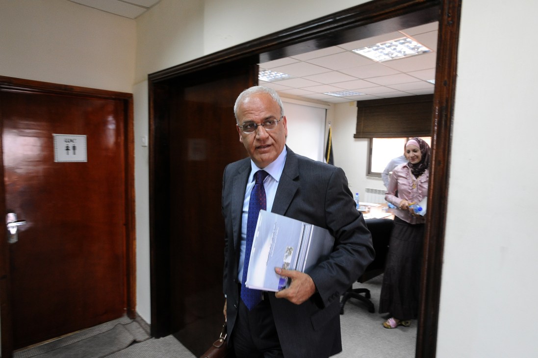 Saeb Erakat, Palestinian chief negotiator, walks through a hallway holding documents while wearing a dark suit and blue tie.