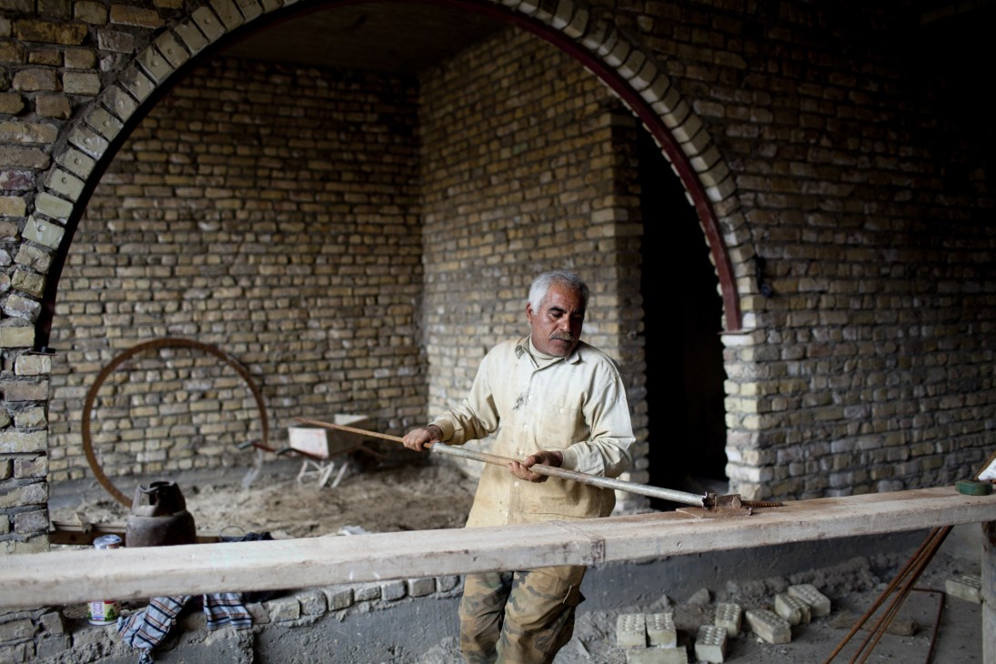 A workman in a light-colored shirt crafts steel bars inside a brick archway.
