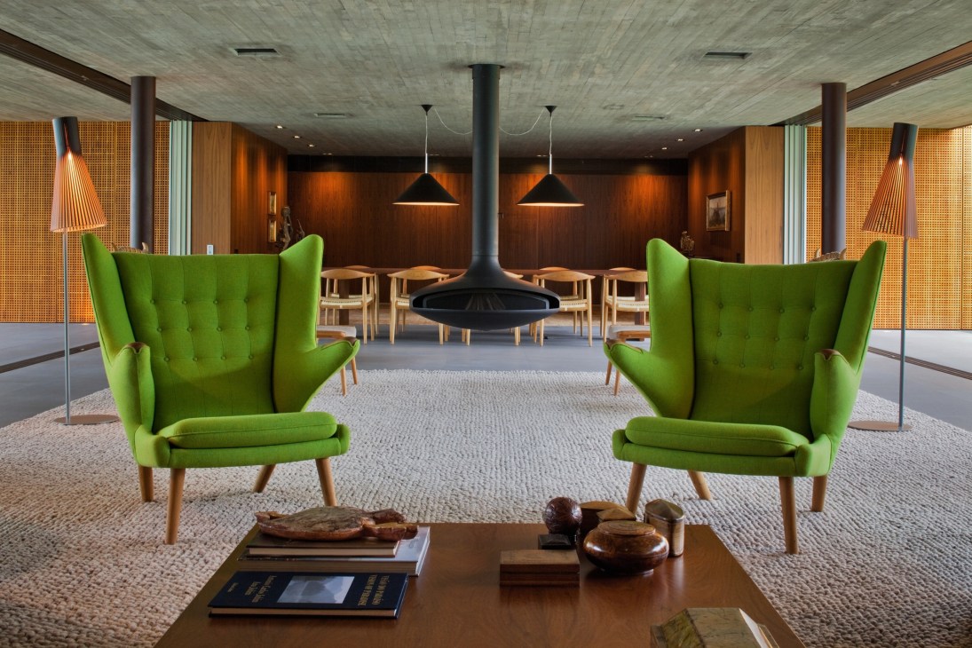 Interior view of V4 residence with green Hans Wegner Teddy Bear Chairs and suspended fireplace in modern living room.