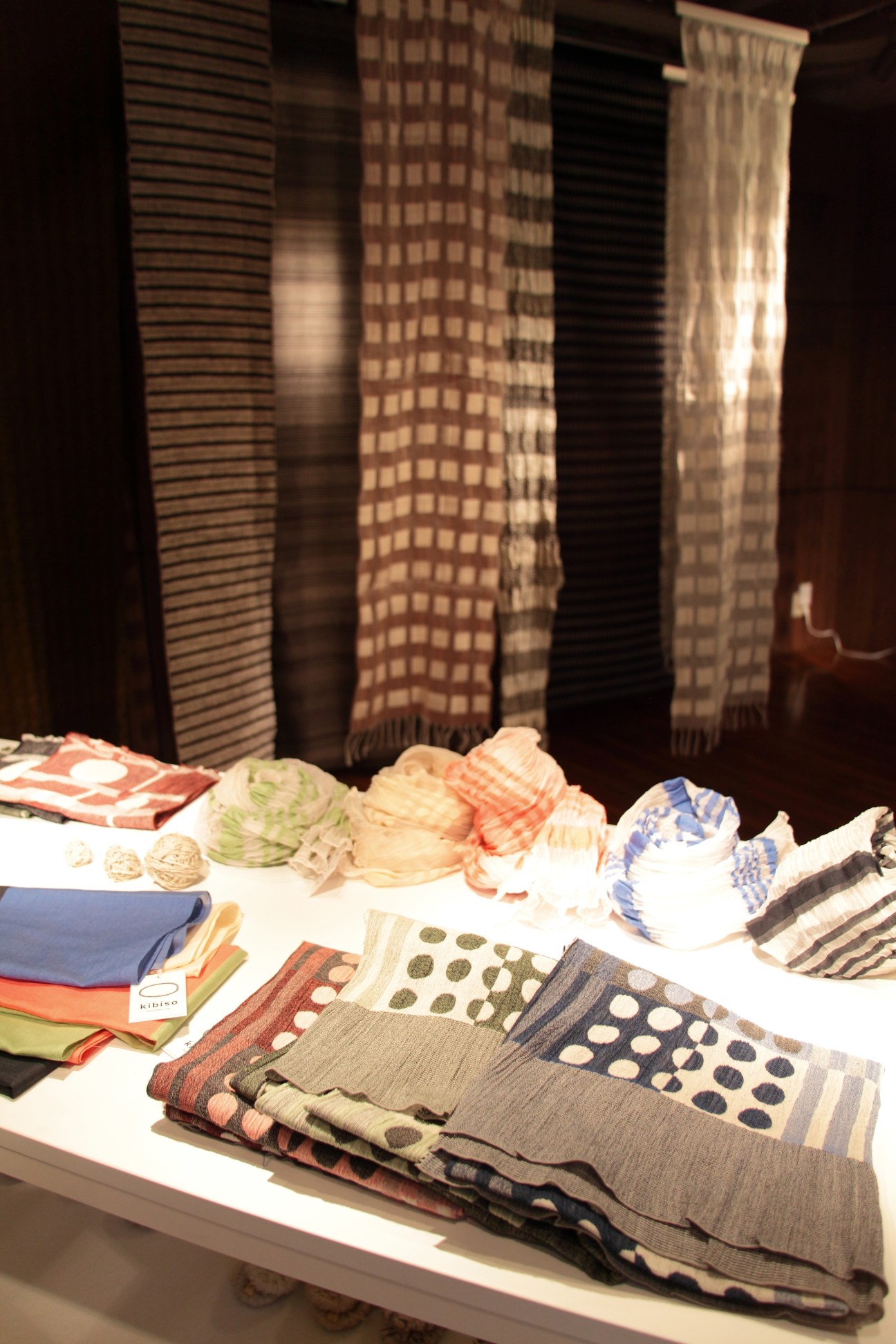 Display of Japanese Kibiso silk textiles with various patterns and colors arranged on a table with woven fabric samples in background.