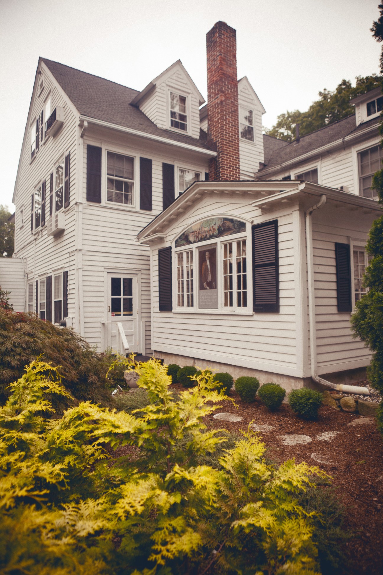 White clapboard exterior of the Roger Sherman Inn with brick chimney and landscaped garden.