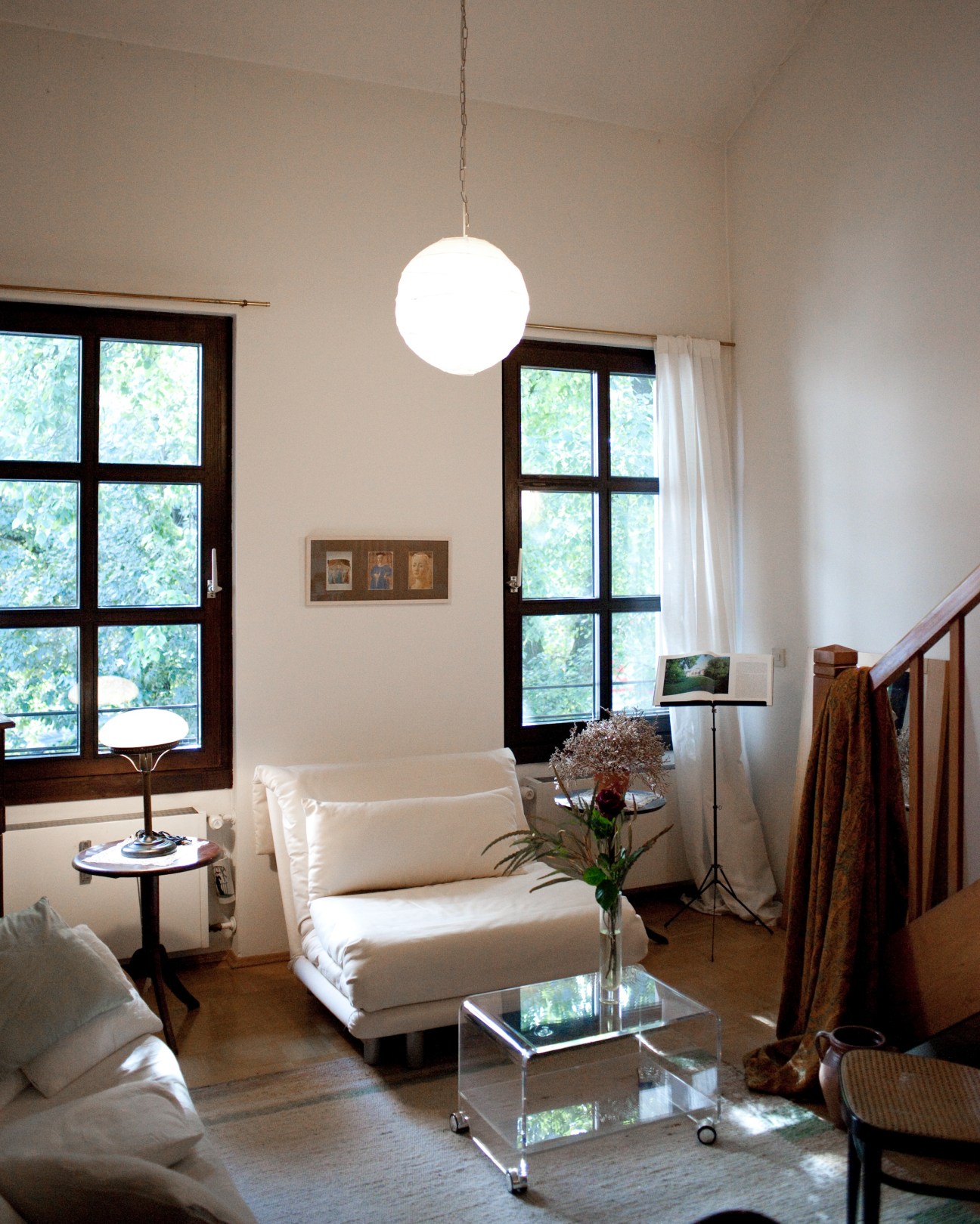 Bright minimalist living room with white furniture, globe pendant light, and dark-framed windows overlooking greenery.