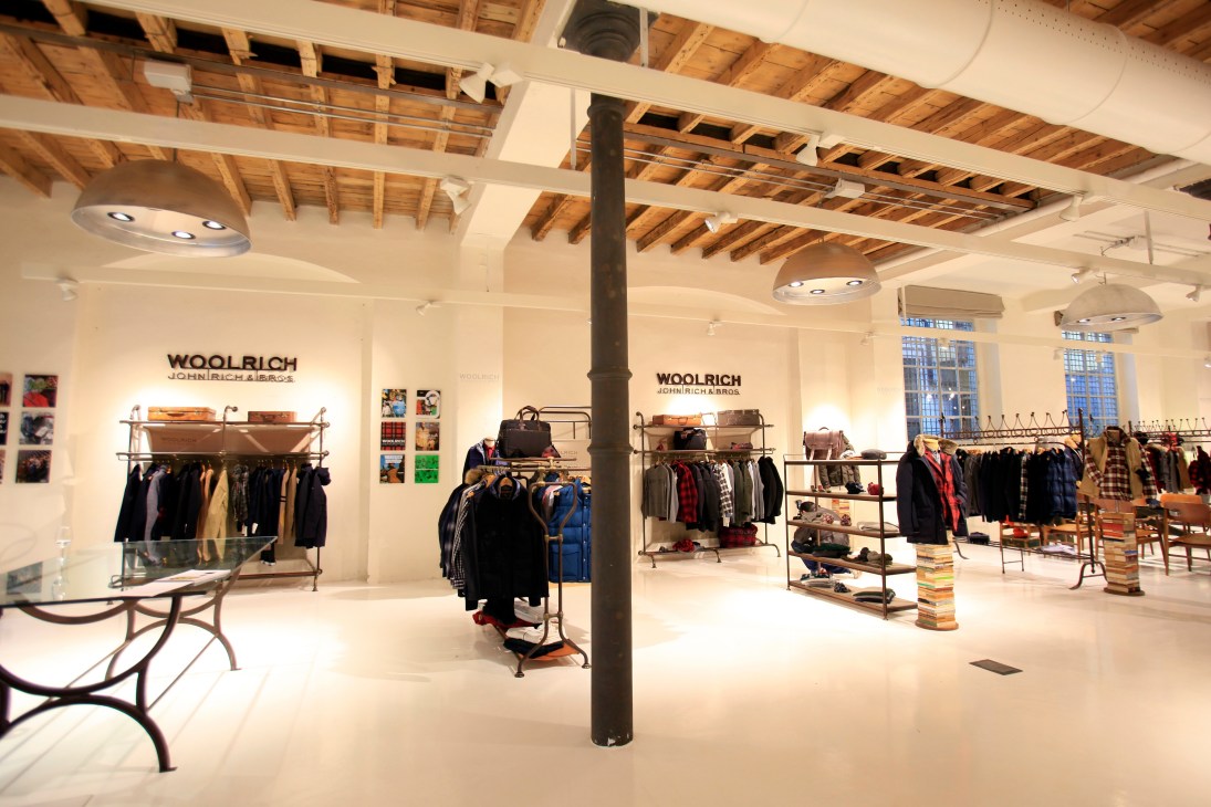 Interior of Woolrich John Rich & Bros store with clothing displays and wooden ceiling beams.