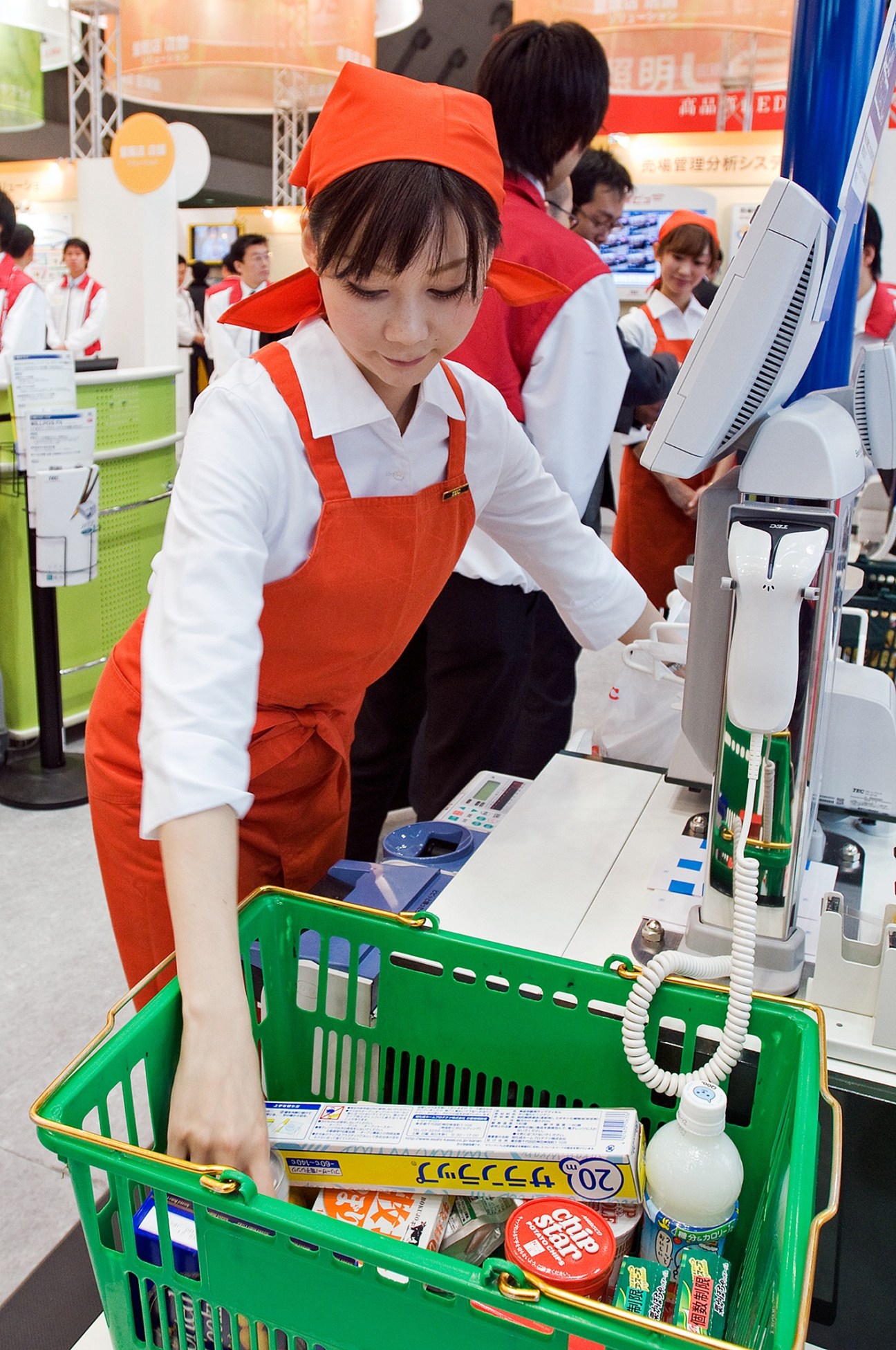Staff member in red apron demonstrating Toshiba's cash register at Japan's Supermarket Trade Show.