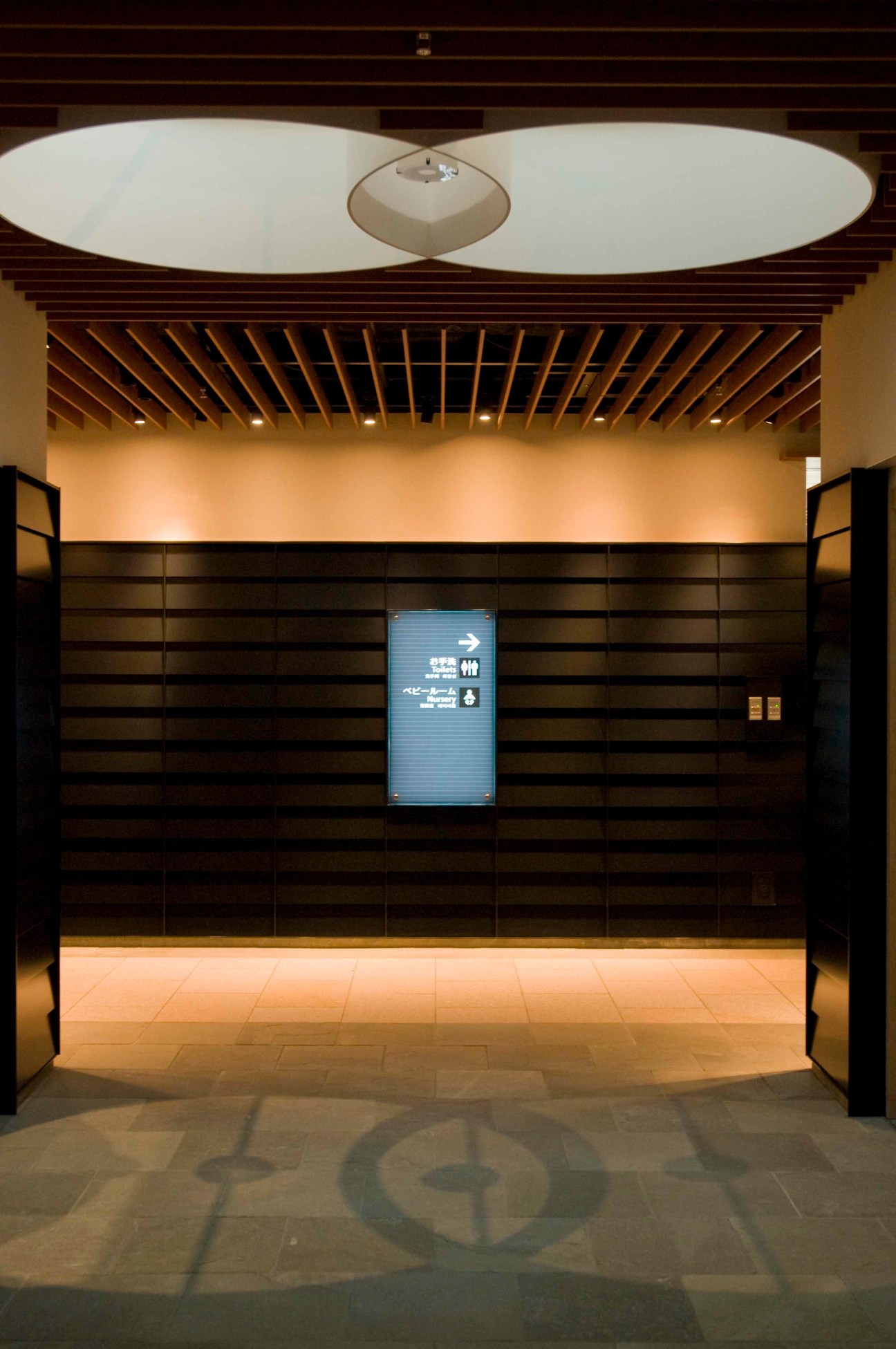 Interior of a Japanese-style storefront with dark wooden lattice panels, warm lighting, and a blue digital sign.