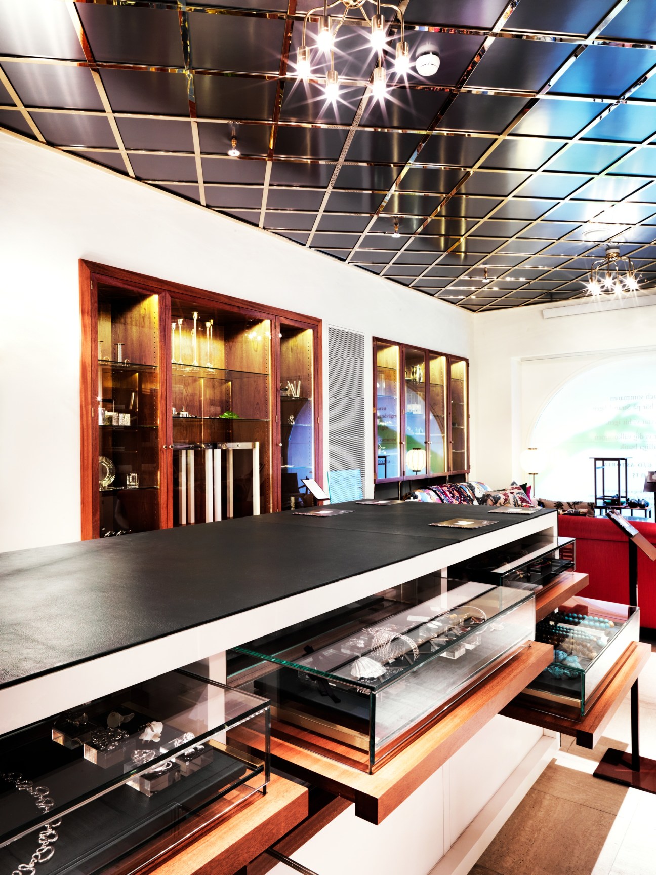 Modern jewellery display cases with dark wood cabinetry and glass shelving beneath a geometric grid ceiling at Svenskt Tenn.
