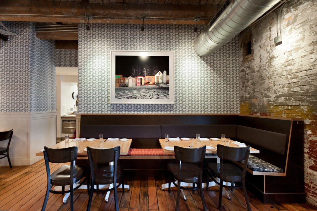 Interior of The Bachelor Farmer restaurant in Minneapolis with patterned wallpaper, wooden table, black chairs, and framed photograph on wall.
