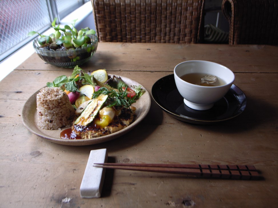 A plated dish with grain, grilled vegetables and salad beside a cup of tea on a wooden table at Starnet in Osaka.