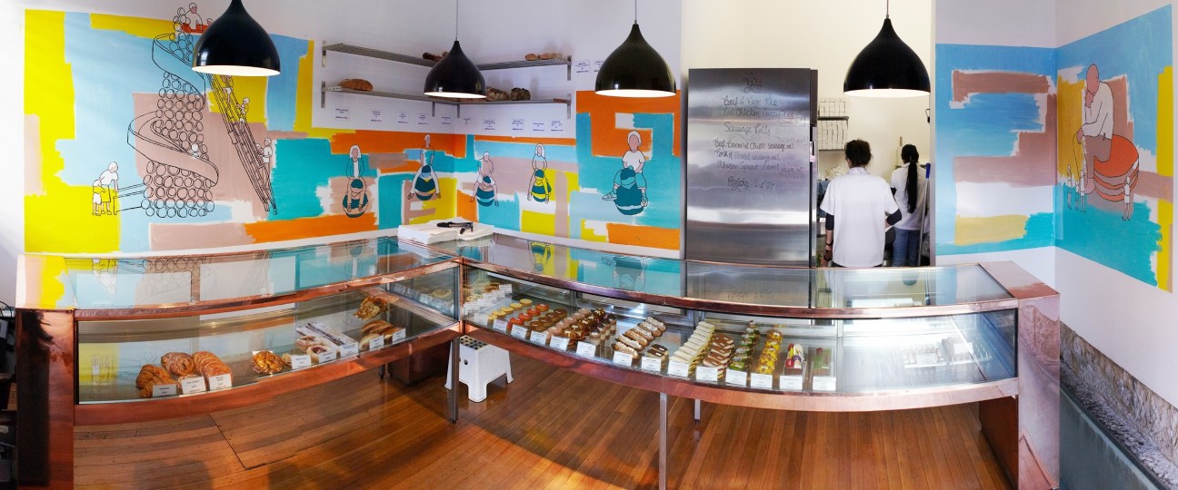 Colorful patisserie display counter with pastries and vibrant mural artwork featuring illustrated figures.